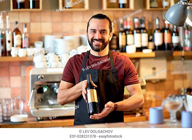 small business, alcohol drinks, people and service concept - happy man or waiter with bottle of red wine at bar
