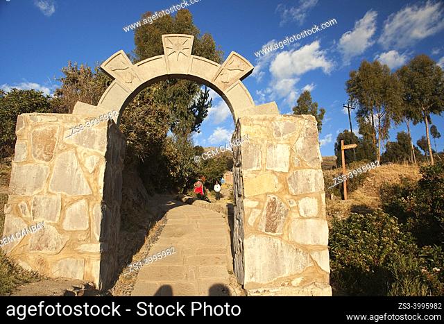 Indigenous people of the island in traditional dress passing through a stone arch and walking up to their house, Amantani Island, Titicaca Lake, Puno Region