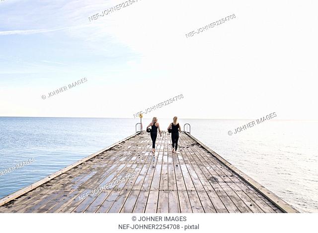 Two women carrying exercise mats, walking on pier