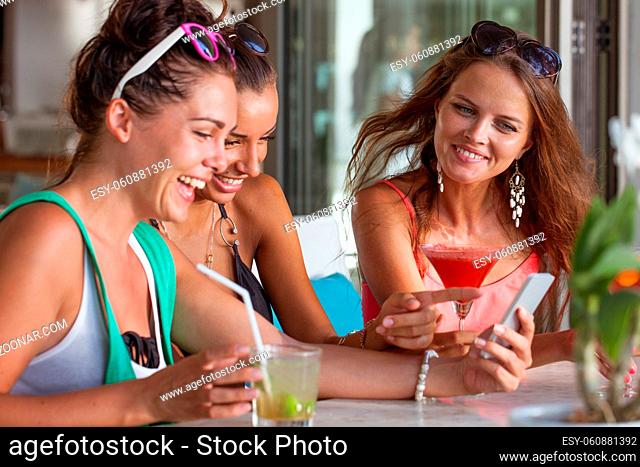 Three friends amazed watching a smart phone sitting in cafe drinking cocktails