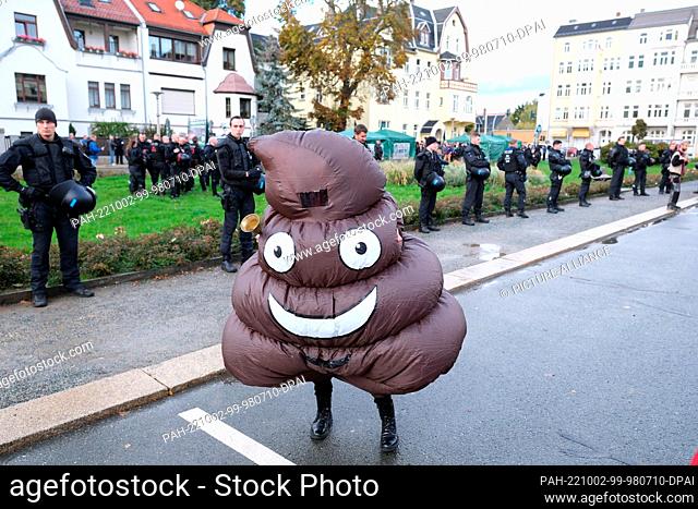 02 October 2022, Saxony, Plauen: A participant of a left-wing demonstration dressed in a suit representing the emoji for ""shit"" and stood at the edge of a...