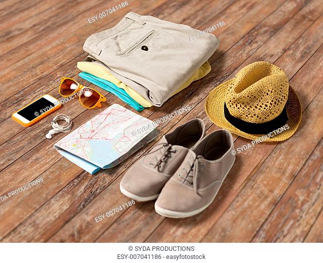 summer vacation, tourism and objects concept - close up of clothes, smartphone, personal stuff and travel map on wooden floor
