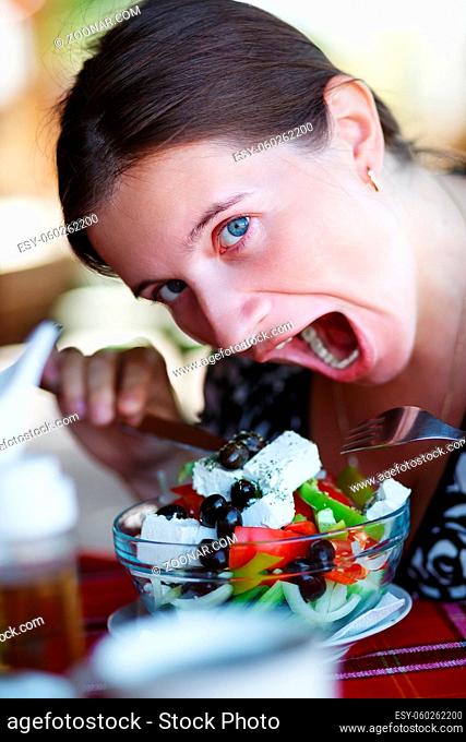 A woman eats a delicious Greek salad. Young woman having fun posing with a plate of salad. Shallow depth of field. Selective focus on the eye of the model