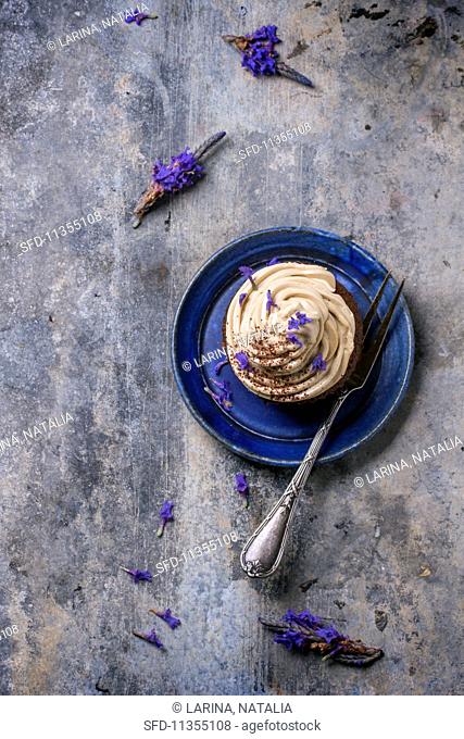 A chocolate cupcake with coffee buttercream and lavender flowers on a blue plate