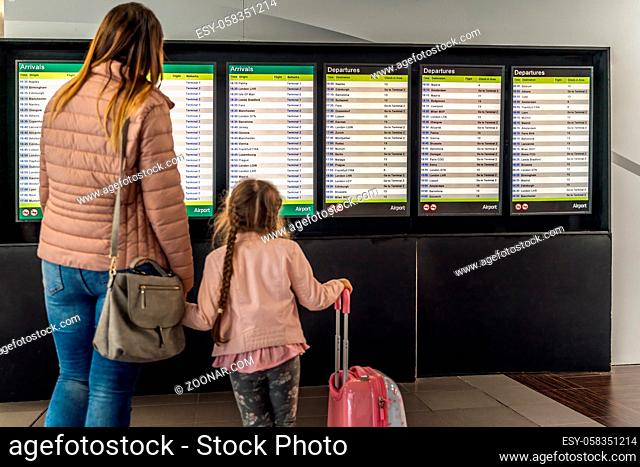 Defocused silhouette of family, young girl and her mother on airport terminal. Checking arrival and departure board for their flight. Dublin, Ireland