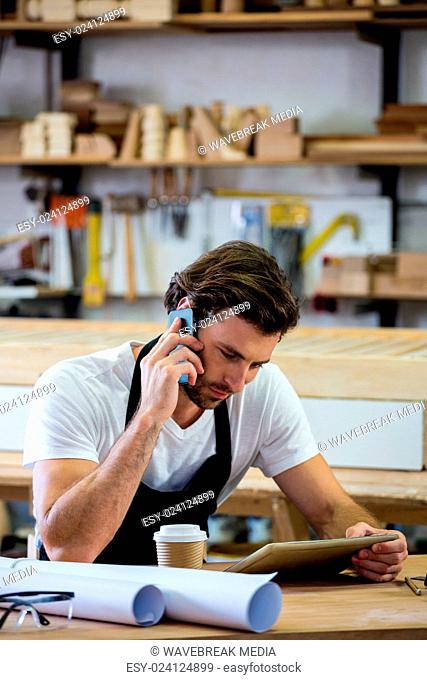 Carpenter calling someone and looking at his tablet