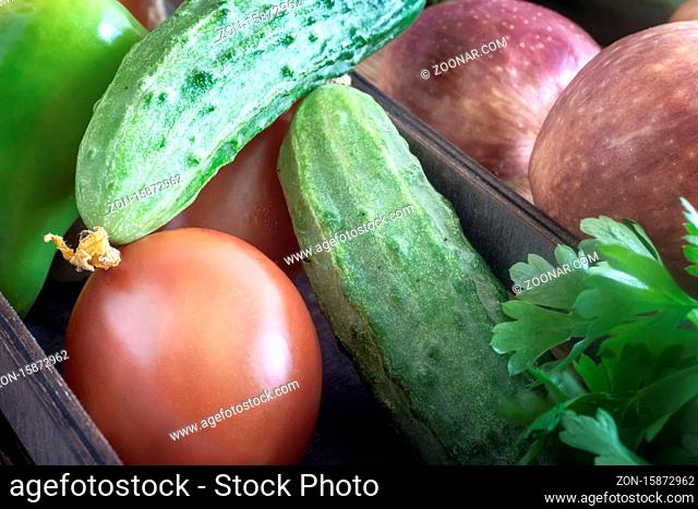 In a small box are cucumbers, tomatoes, apples. Presented in close-up