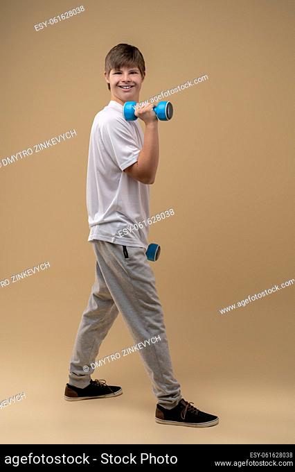 Full-length portrait of a smiling happy teenager with dumbbells in his hands posing for the camera