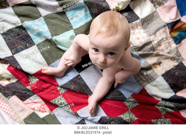 Caucasian baby boy sitting on blanket looking up