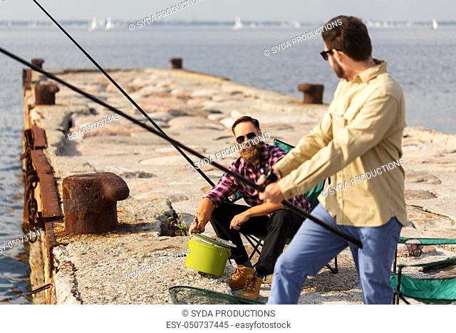 male friends with fishing rods on sea pier