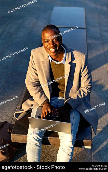 Businessman smiling sitting with laptop on bench