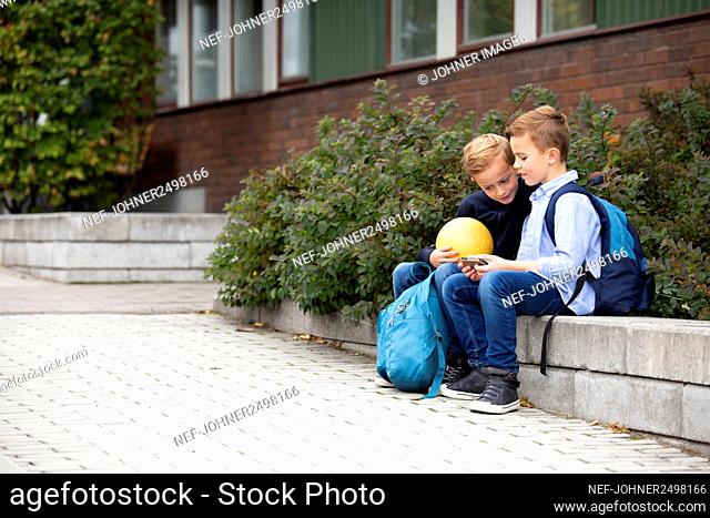 Boys looking at cell phone in front of school building