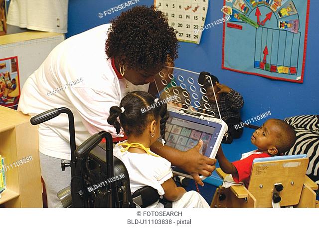Teacher with two children with multiple disabilities, explaining and demonstrating how to use a communication device