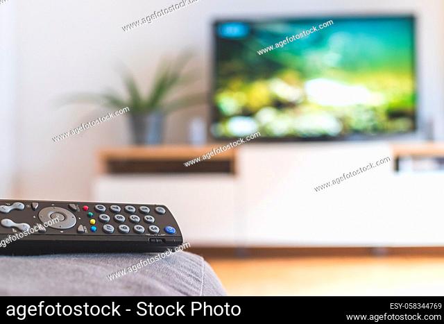 TV remote control in the foreground, tv in the blurry background. Streaming