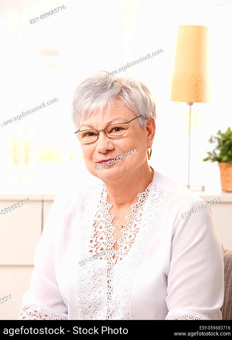 Portrait of pensioner woman sitting in living room, looking at camera, smiling