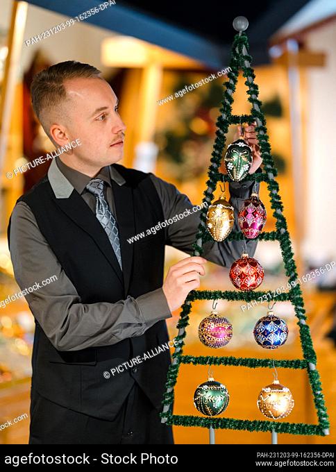 PRODUCTION - 30 November 2023, Thuringia, Lauscha: Tobias Greiner-Lar, an employee at Krebs-Glas, attaches colored Christmas tree baubles from the ""Jewels""...