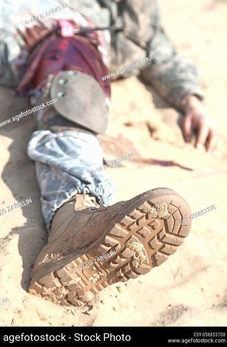 Injured airborne infantry paratrooper shot in leg hip on desert sand. Blood spilled but tourniquet is on, he will be alive