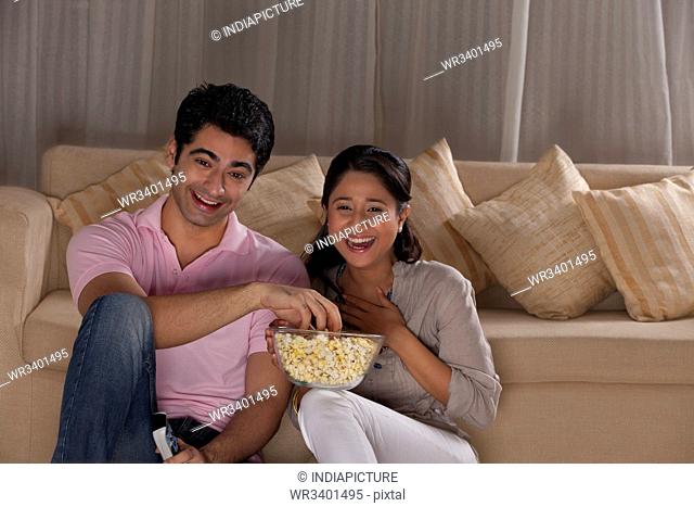 Happy young couple enjoying while watching TV at home