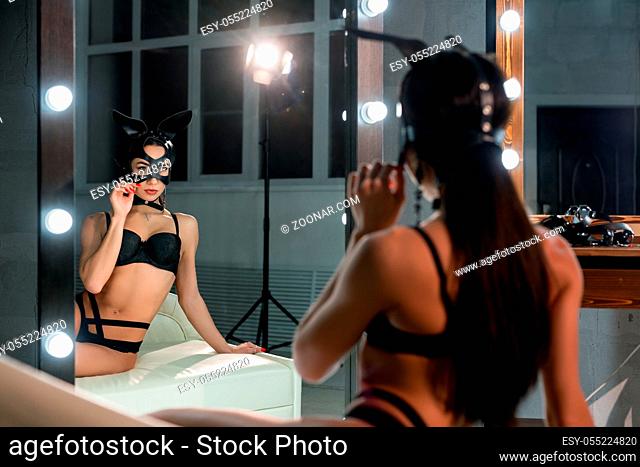Woman in mask and bunny ears wearing black lingerie cropped rearview against mirror