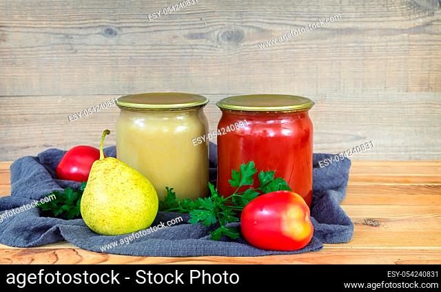 Pear puree and tomato juice are preserved in glass jars with sealed metal lids. Near lie pears and tomatoes