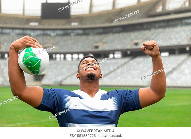 Happy African American Rugby player cheering with the ball in the stadium