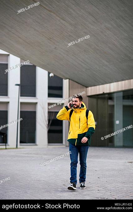 Smiling man on thephone walking along building in the city