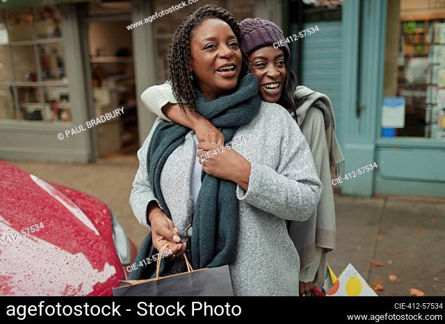 Happy mother and daughter with shopping bags on sidewalk
