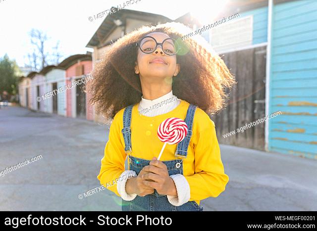 Girl wearing eyeglasses holding lollipop on sunny day
