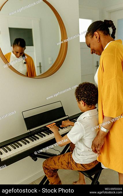 Smiling woman looking at son playing piano at home