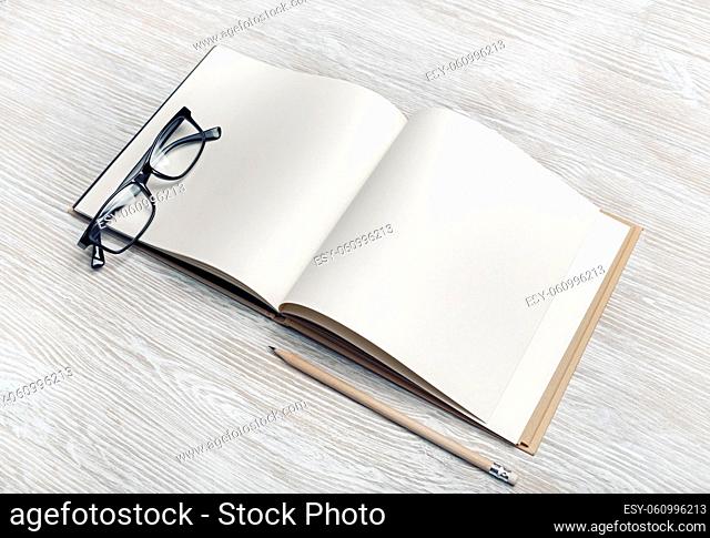 Photo of blank brochure, pencil and glasses on light wooden background. Responsive design mockup. Stationery elements. Template for placing your design