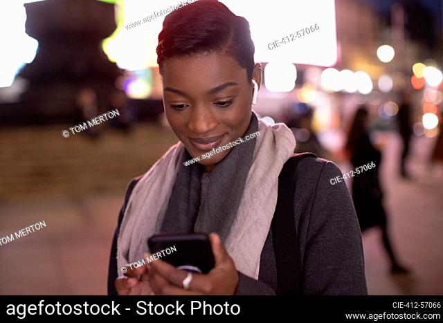Young woman using smart phone on city sidewalk at night