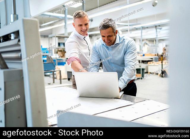 Two smiling colleagues using laptop in a factory