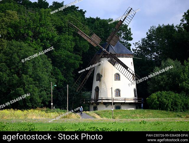 26 July 2023, Saxony, Dresden: A cyclist passes the Gohlis windmill on the Elbe cycle path in the morning. The mill was built from 1828 to 1832