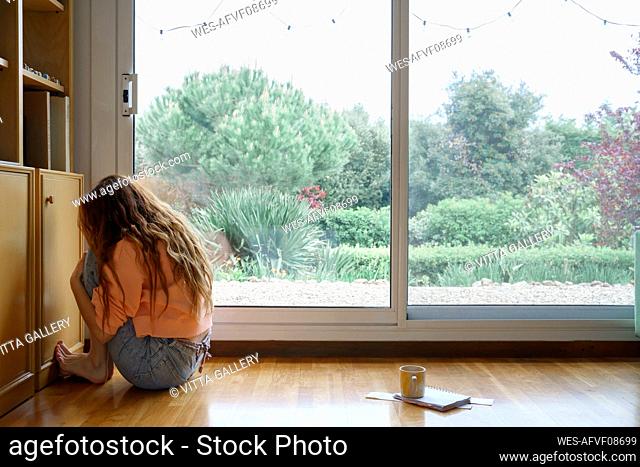 Sad woman with long hair sitting while hugging knees at home