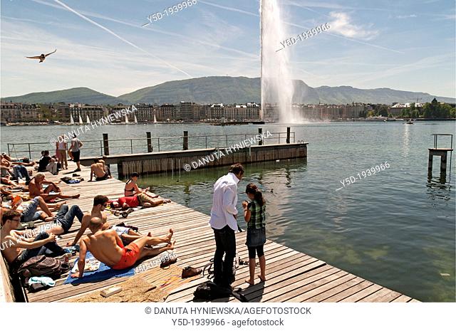 people resting at the shore of Geneva Lake, Paquis beach, famous fountain Jet d'Eau in the background, Geneva, Switzerland, Europe