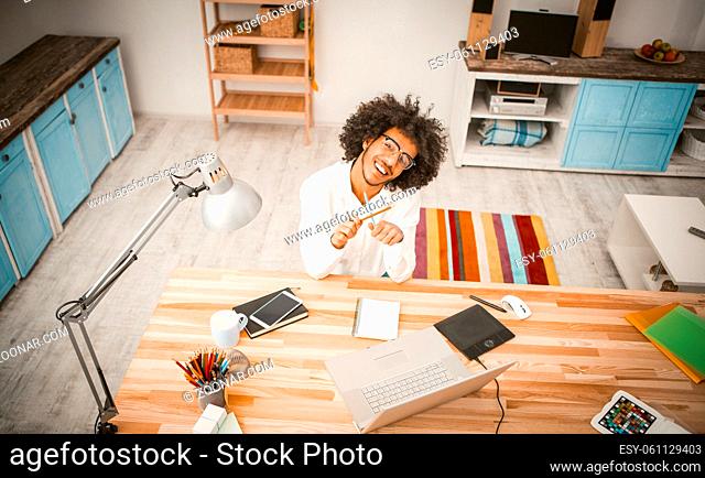 Jolly young businessman took break from work. Cheerful arab guy play with pencils looking at camera while sitting at workplace in studio room
