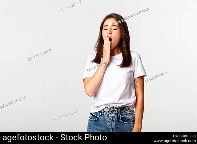 Portrait of attractive young female student yawning tired, feeling sleepy, white background