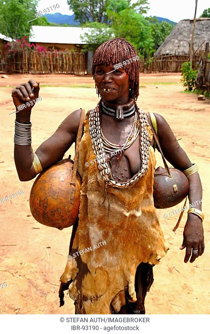 Woman of the Hamar people wears a leather cloth and typical clay hairdo a metal and kauri mussel chain and kalabasses at the market of Dimeka Ethiopia