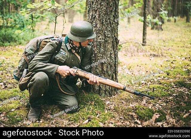 Hidden unidentified re-enactor dressed as World War II german wehrmacht soldier sitting with rifle in an ambush in forest