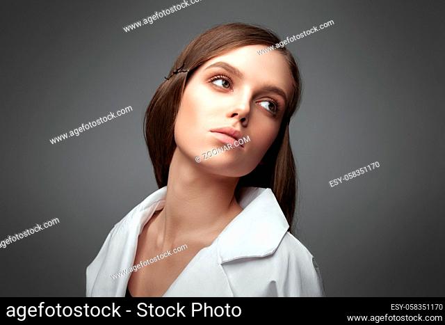 Portrait of a beautiful European fashion model wearing white blouse on a gray background. Beautiful hair and perfect skin