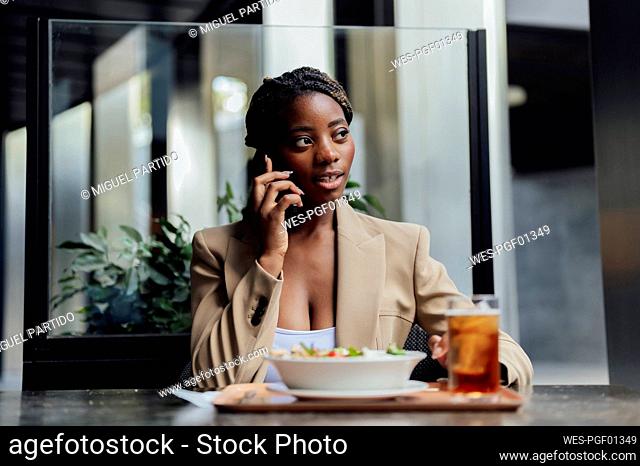 Young businesswoman talking on smart phone sitting at cafeteria