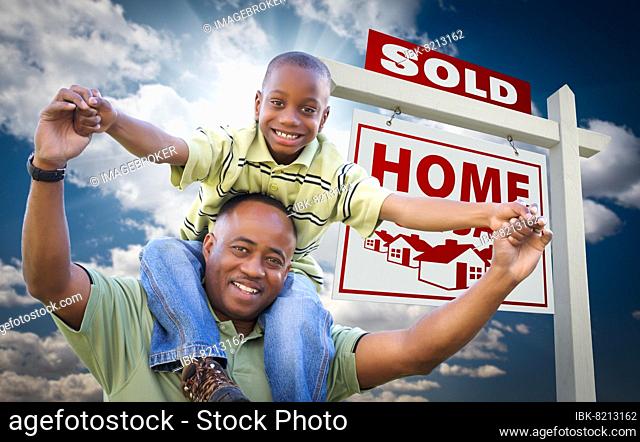 Happy african american father with son in front of sold home for sale real estate sign and sky