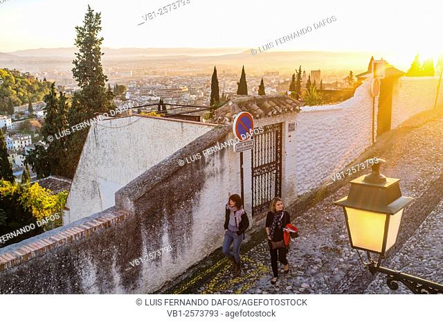 Couple walking at sunset through the alleys of the Moorish Albaicin quarter with Granada overview in background. Granada, Spain
