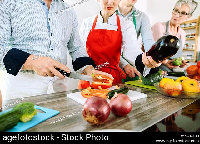 Man in training kitchen cutting vegetables under watchful eye of competent dietician