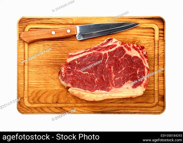 Close up one marbled raw ribeye beef steak with rib bone on wooden cutting board with knife, isolated on white background, elevated top view, directly above