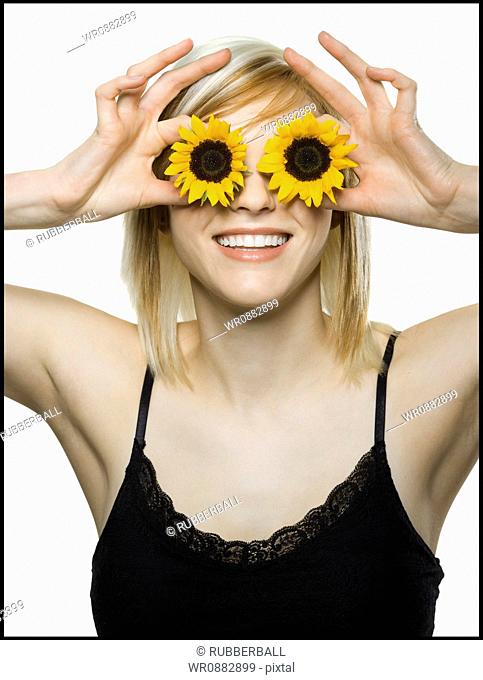 Close-up of a young woman holding sunflowers in front of her eyes