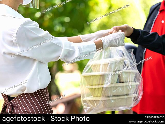 Close up waitress hand give food box to deliverly man to deliver it to customer make online order. Food deliverly service concept in new normal after...