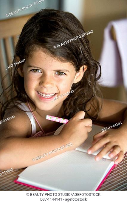 Little caucasian girl writing on a notebook smiling
