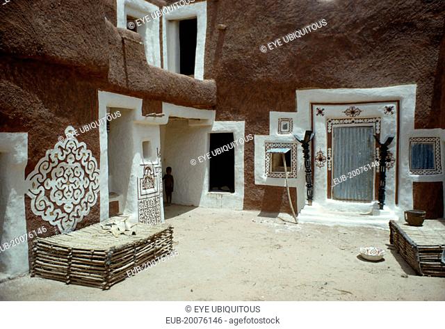 Traditional mud architecture decorated with bas relief motifs of applied gypsum, white and red clay. Small child standing in shadow of corner of building