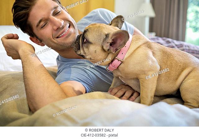 Dog licking man's face on bed